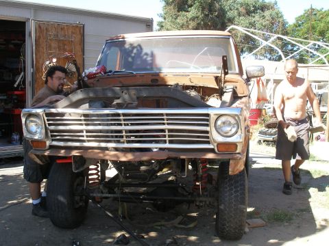 1969 Ford F-250 - A mechanic works on the engine of a 1967 Ford F-series pickup truck, which is missing its hood and appears to be undergoing repairs or modi…