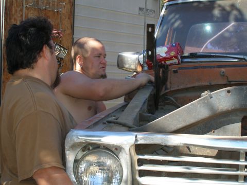 1969 Ford F-250 - Two men are gathered around the open hood of a truck, appearing to work on the engine. The truck's front end is visible.