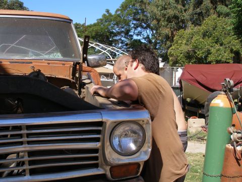 1969 Ford F-250 - Two individuals examine the engine bay of a 1969 Ford F-250, its distinctive grille visible.