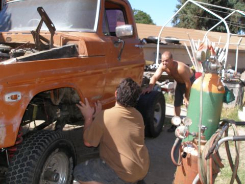 1969 Ford F-250 - Two men work on an orange pickup truck, with welding equipment visible in the foreground.