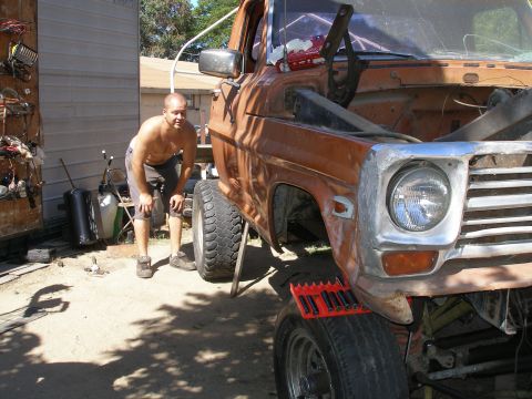 1969 Ford F-250 - A man inspects the front end of an orange pickup truck that is raised on a jack.
