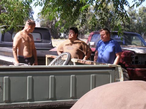 1969 Ford F-250 - Three men are gathered around the beds of pickup trucks in an outdoor setting.
