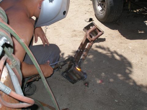 1969 Ford F-250 - A person is using a torch to cut a metal frame part, with a vehicle tire in the background.