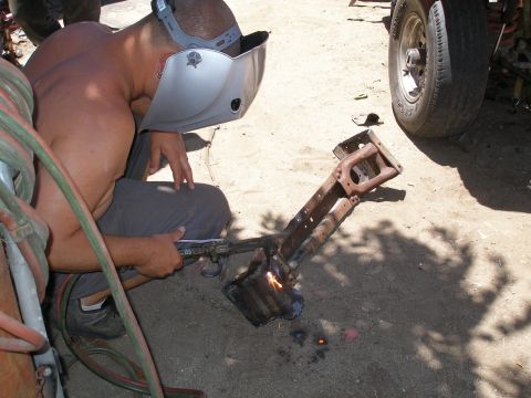 1969 Ford F-250 - A man is welding a section of a truck frame, with a tire and part of the vehicle visible.