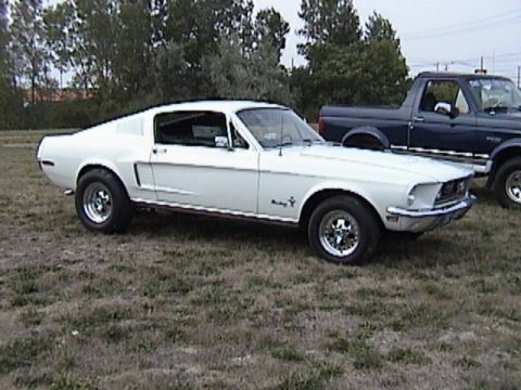 1968 Ford Mustang - A white 1968 Ford Mustang fastback is parked on a grassy field next to a dark blue pickup truck.