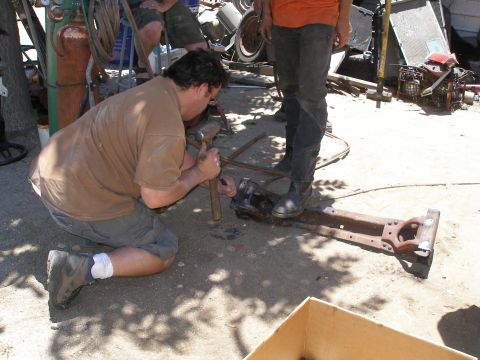 1969 Ford F-250 - Men are working on a vehicle frame in a junkyard setting, with various parts and equipment visible.