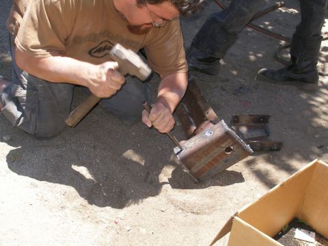 1969 Ford F-250 - A person uses a hammer and chisel on a rusty metal bracket.