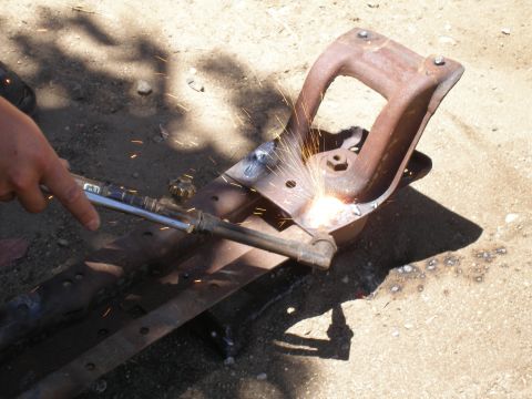 1969 Ford F-250 - A close-up view of a person using a torch to weld a rusty, cast iron suspension part, with sparks flying.
