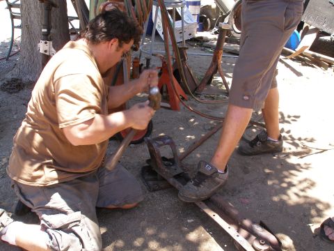 1969 Ford F-250 - Two men are working on a metal part outdoors, using hammers and other tools.