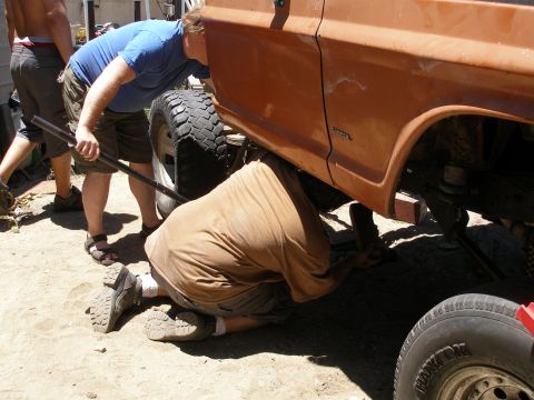 1969 Ford F-250 - Mechanics work on the underside of an orange truck with a lifted suspension and large tires.
