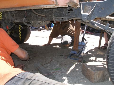 1969 Ford F-250 - Mechanics work on the underside of a truck, with a jack lifting the frame for repairs.