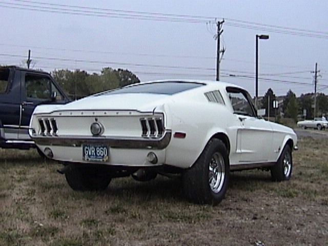 White Mustang fastback rear view with chrome bumper and mag wheels parked on grass