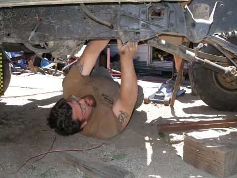 1969 Ford F-250 - A mechanic is seen working on the underside of a truck chassis, with tools and equipment around.