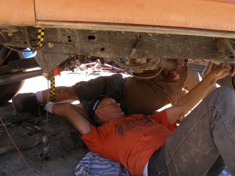 1969 Ford F-250 - Mechanics work on the undercarriage of a vehicle, with tools and parts scattered around.
