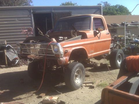 1969 Ford F-250 - This orange pickup truck is undergoing modifications with its hood open and lifted suspension.