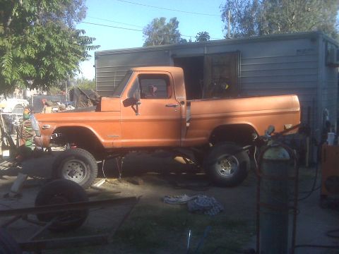 1969 Ford F-250 - This orange pickup truck features a lifted suspension and appears to be undergoing modifications or repairs.