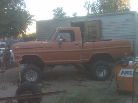 1969 Ford F-250 - This orange pickup truck has a lifted suspension and appears to be undergoing some work.