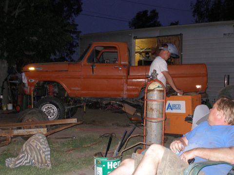 1969 Ford F-250 - An orange 1967 Ford F-100 pickup truck with a lifted suspension is seen in a yard, appearing to be under repair or modification.