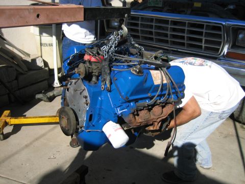 1979 Ford F-150 - An engine is being removed from a vehicle using an engine hoist. The engine is blue and has a white oil filter.