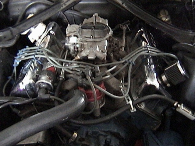 V8 engine bay with exposed four-barrel carburetor and chrome valve covers