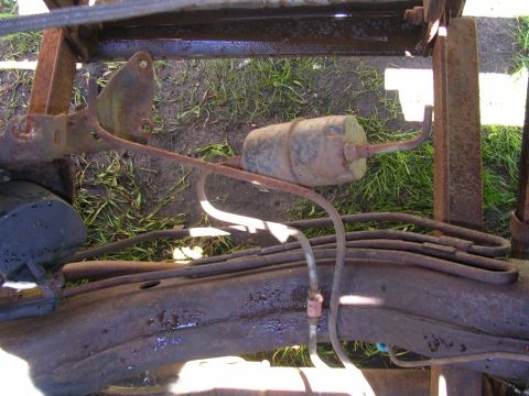 1978 Ford Bronco - The undercarriage of a vehicle displays a rusty fuel filter and brake lines, with grass visible below.