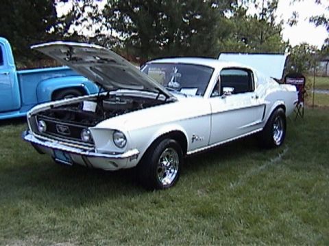 1968 Ford Mustang - A white 1968 Ford Mustang coupe is displayed with its hood open, next to a blue pickup truck.