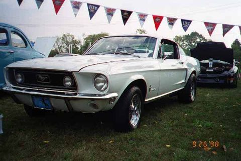 1968 Ford Mustang - A white 1968 Ford Mustang is parked on grass with a blue license plate and other cars in the background.