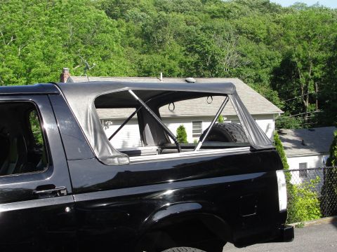 1995 Ford Bronco - Side view of a black SUV with a soft top, showing the rear cargo area and a spare tire.