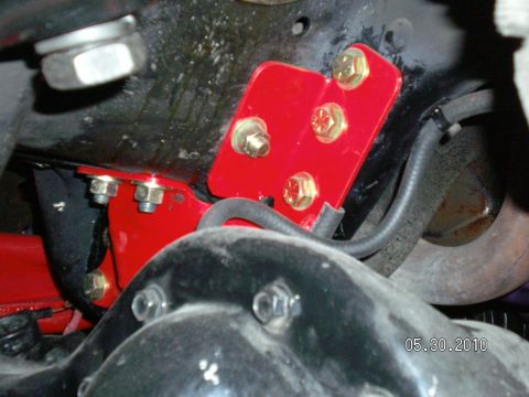 1996 Ford Bronco - Close-up view of a red suspension bracket and hardware on a vehicle's undercarriage.