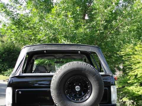1995 Ford Bronco - Rear view of a black SUV with a soft top and a spare tire mounted on the tailgate.