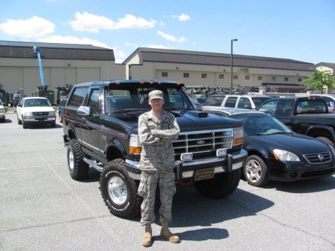 1995 Ford Bronco - A person in military uniform stands next to a lifted black Ford Bronco in a parking lot.