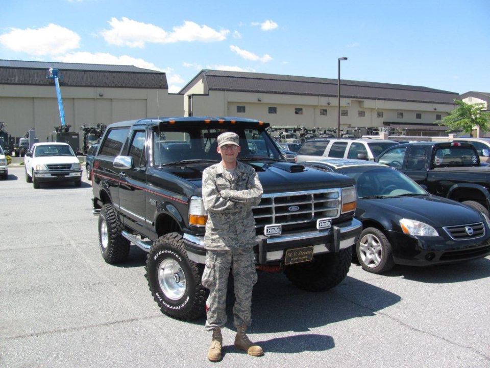 Black lifted Ford Bronco with large tires, front view. Person in uniform stands beside it