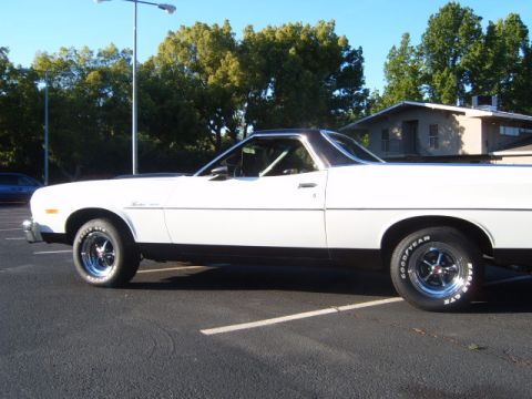 1973 Ford Ranchero - A white 1973 Ford Ranchero is parked in a lot under a street light, with trees and a house in the background.