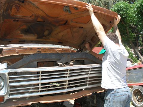 1969 Ford F-250 - Man opens the hood of a rusty orange truck with a prominent chrome grille.
