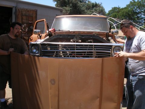 1969 Ford F-250 - Two men hold a large piece of cardboard in front of a truck's grille, obscuring the lower half of the vehicle.