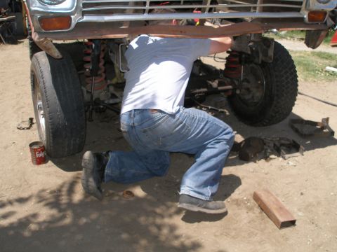 1969 Ford F-250 - A person kneels to work on the underside of a large vehicle, with parts scattered on the ground.