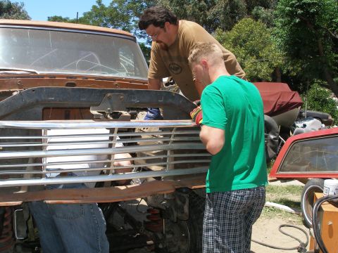 1969 Ford F-250 - Two men are working on the front grille of a rusty truck, possibly during a repair or restoration.
