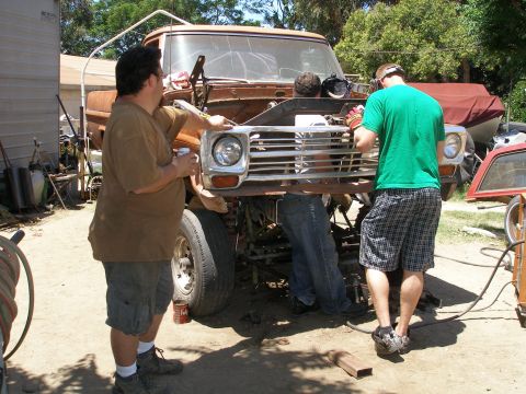 1969 Ford F-250 - Two men work on the front of a rusty 1967 Ford F-Series truck, with the hood open and grille exposed.