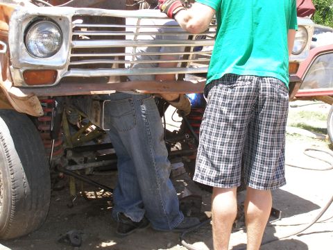 1969 Ford F-250 - Mechanics work on the front end of a truck, with the grille and headlight visible.