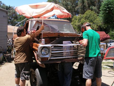 1969 Ford F-250 - Men are working on a rusty pickup truck, one is welding. The truck appears to be from the late 1960s.