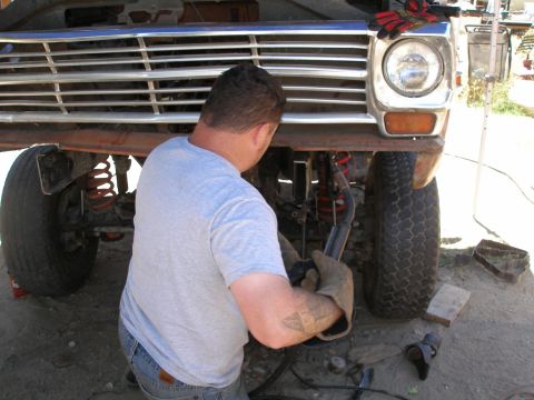 1969 Ford F-250 - A mechanic works on the front end of a vintage Ford F-100 pickup truck, with the grille and headlight clearly visible.