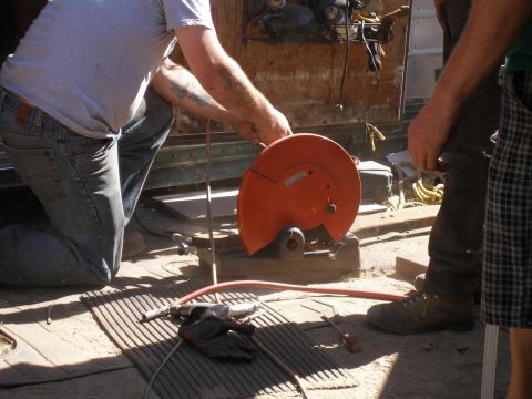 1969 Ford F-250 - A person operates a chop saw, cutting metal outdoors with assistance.
