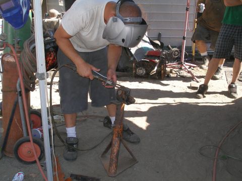 1969 Ford F-250 - A man is welding metal outdoors, with various tools and scrap metal visible in the background.
