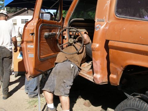 1969 Ford F-250 - A man works on the steering wheel of an orange truck, with the driver's side door open.
