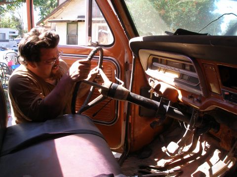 1969 Ford F-250 - A man works on the steering column inside the cab of a 1967 Ford F-Series truck.