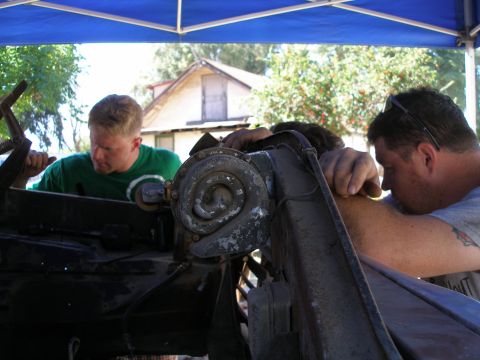 1969 Ford F-250 - Mechanics are focused on the engine of a vehicle, working outdoors under a blue tarp.