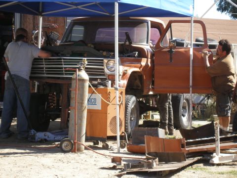 1969 Ford F-250 - Two men work on an orange truck that is elevated on a lift, with tools and equipment around.