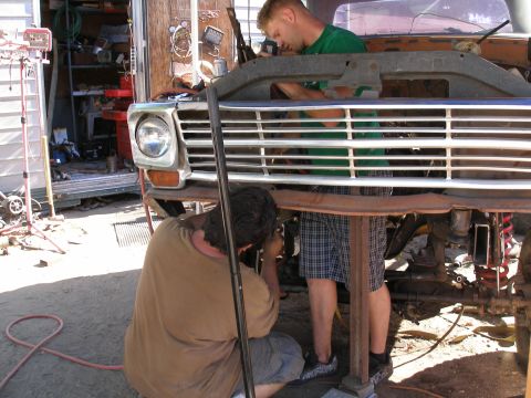 1969 Ford F-250 - Two mechanics work on the front end of a truck, focusing on the grille and headlight assembly.