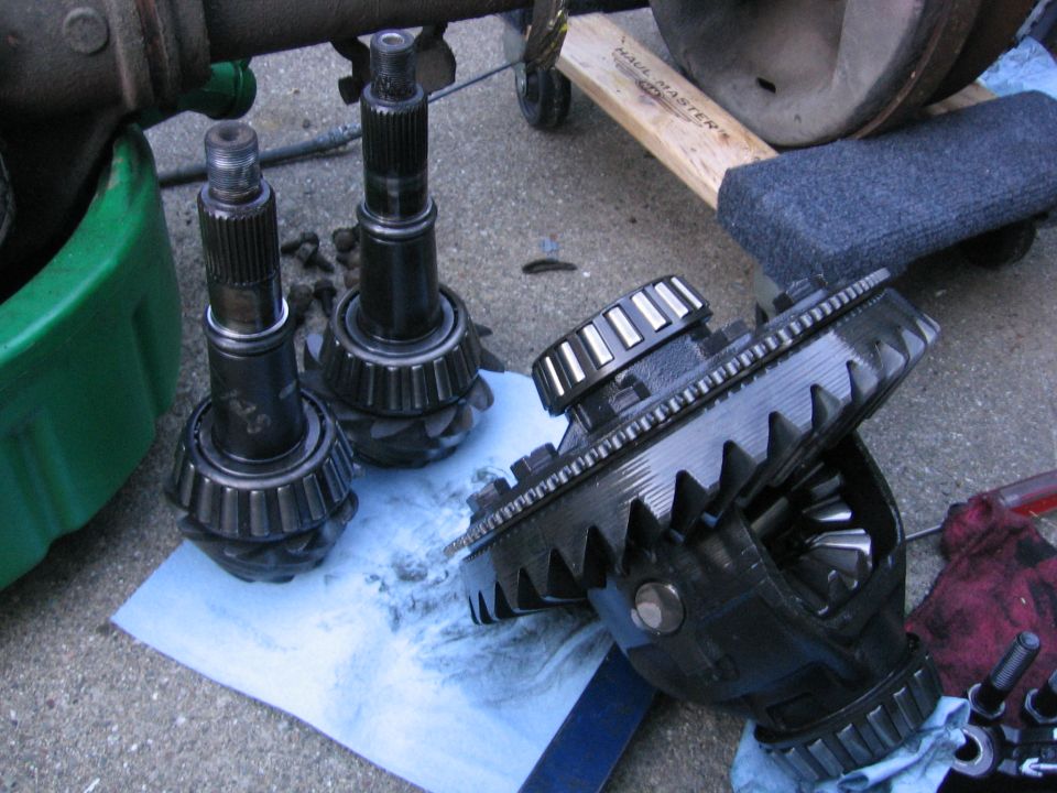 Differential gears and axles laid out on a driveway, some in a green pan