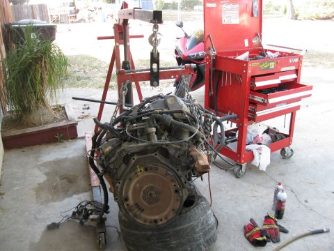 1969 Ford F-250 - An engine is suspended by a red engine hoist, with a red toolbox and a motorcycle in the background.